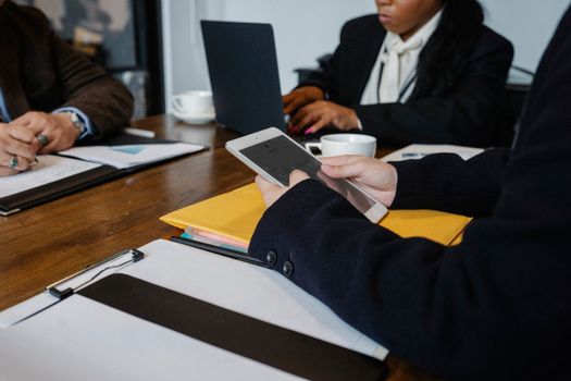 Crop faceless coworkers in formal wear gathering at table with gadgets and documents for brainstorm